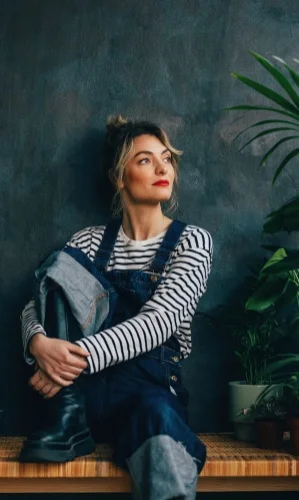 A smiling Caucasian female sitting on the bench, among her houseplants.